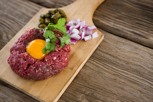 Minced meat with egg yolk, onions and olives on wooden tray against wooden background
