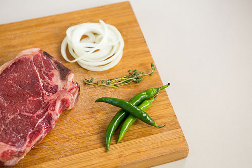 Sirloin chop, herbs and chillies on wooden tray against white background