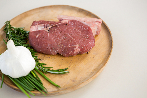 Sirloin chop, rosemary herb and garlic on wooden tray against white background