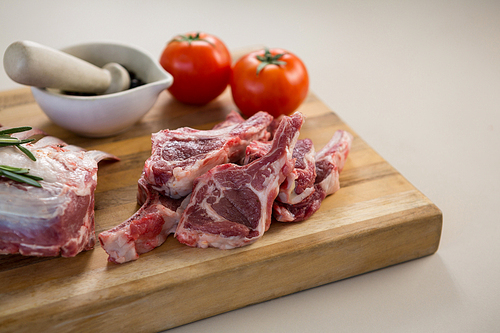 Rib chop, stone grinder and tomatoes on wooden board against white background