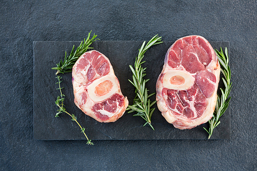 Sirloin chops and rosemary herb on slate plate against black background