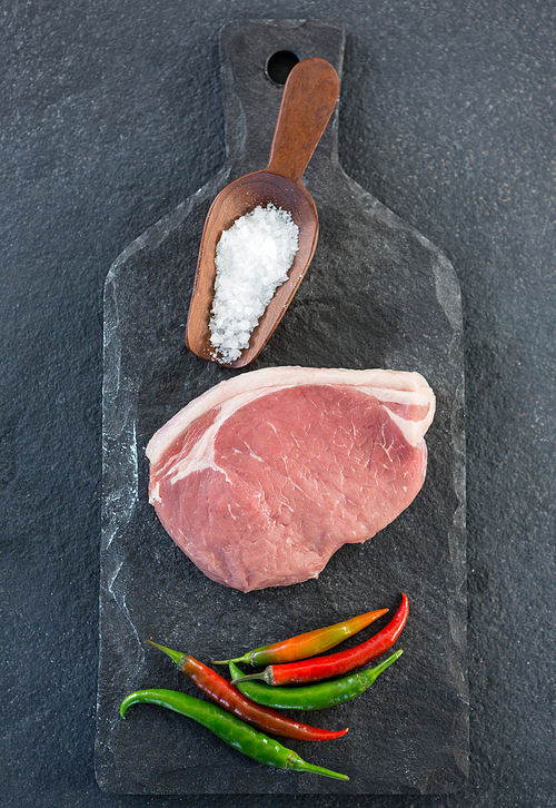 Sirloin chop, salt and chillies on slate plate against black background