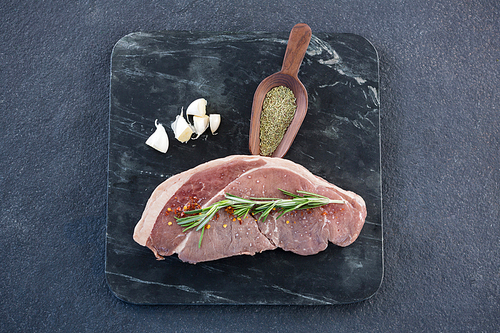 Sirloin chop, spics and garlic on slate plate against black background