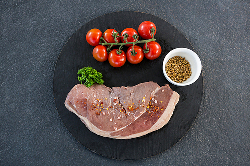 Sirloin chop, cherry tomatoes and coriander seeds against black background