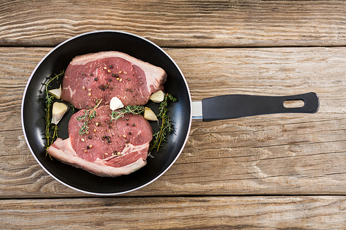Sirloin chops and herbs in frying pan against wooden background
