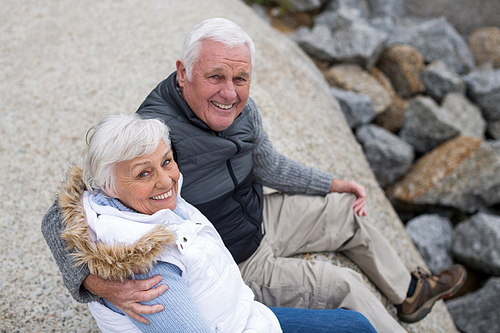 Portrait of happy senior couple sitting on rock at beach