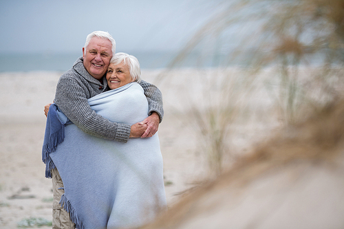 Happy senior couple wrapped in shawl on the beach