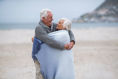 Happy senior couple wrapped in shawl on the beach