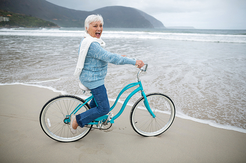 Happy senior woman riding bicycle on the beach
