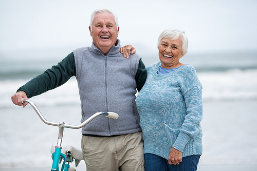 Portrait of senior couple standing with bicycle on the beach