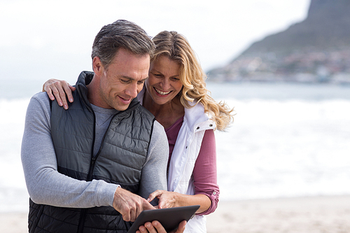 Happy mature couple using digital table on the beach