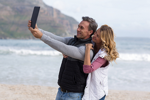 Mature couple taking selfie with digital tablet on the beach
