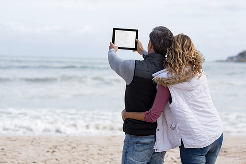 Rear view of mature couple taking selfie with digital tablet on the beach