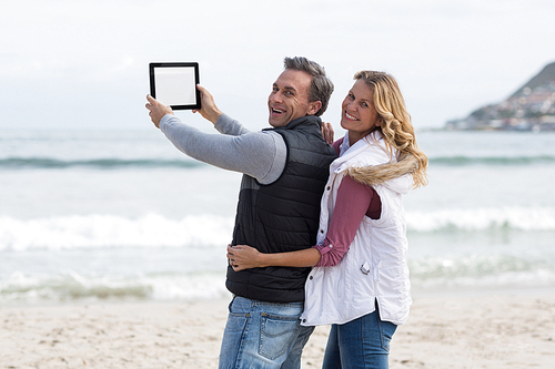 Portrait of mature couple taking selfie with digital tablet on the beach