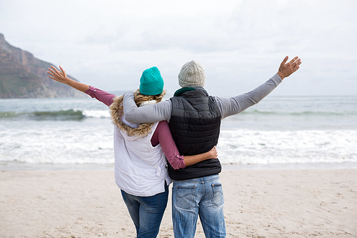 Rear view of mature couple standing with arms outstretched on the beach