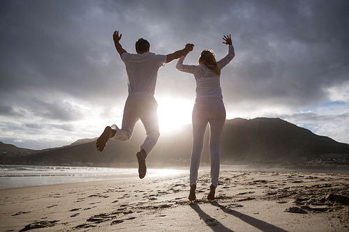 Rear view of mature couple jumping in air on the beach