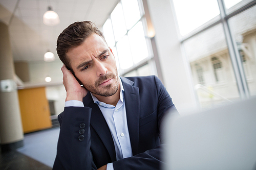 Worried businessman sitting at desk with laptop in conference centre