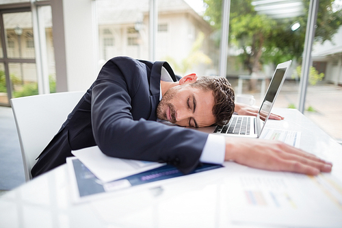 Tired businessman resting head on desk at conference centre
