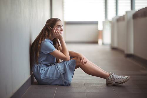 Sad schoolgirl sitting in corridor of school