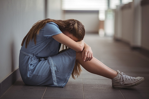 Sad schoolgirl sitting in corridor of school