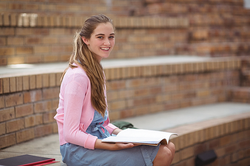 Portrait of schoolgirl reading book in campus at school