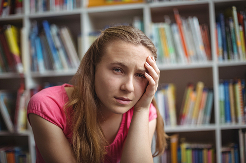 Portrait of sad schoolgirl sitting in library at school