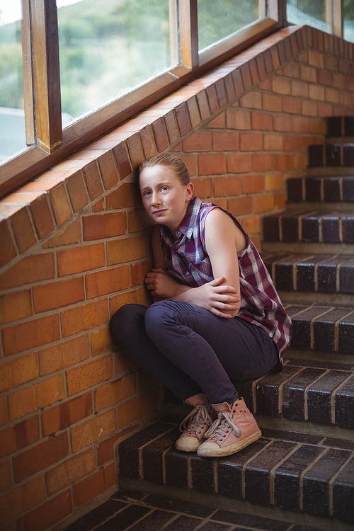 Sad schoolgirl sitting alone on staircase in school