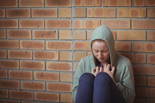 Sad schoolgirl sitting alone against brick wall in school