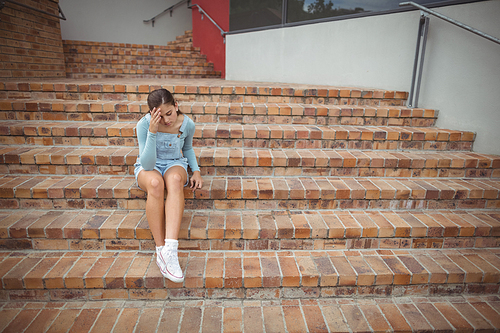 Sad schoolgirl sitting alone on staircase in school campus