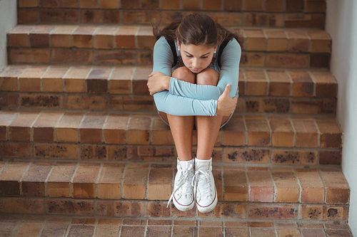 Sad schoolgirl sitting alone on staircase in school