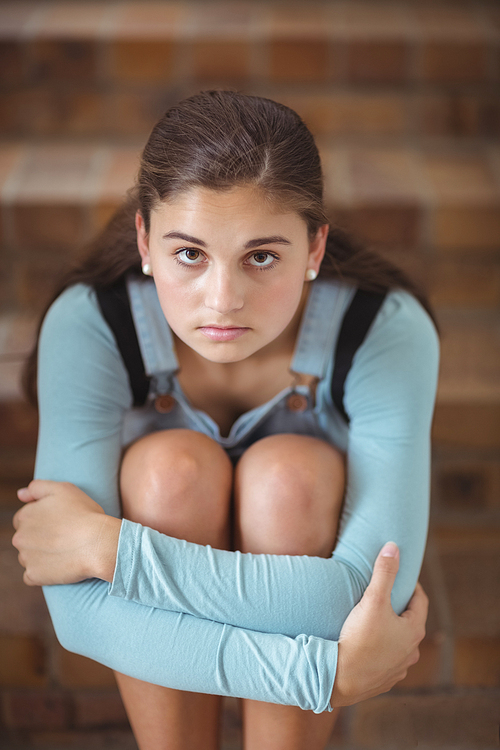 Portrait of sad schoolgirl sitting alone on staircase in school