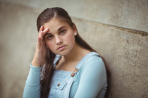 Portrait of anxious teenage girl leaning on wall at school
