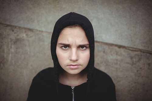 Portrait of anxious teenage girl in black hooded jacket standing at school