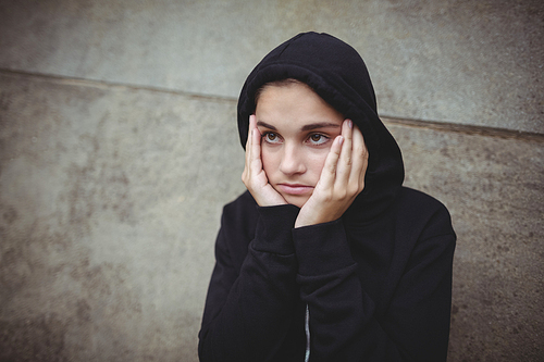 Anxious teenage girl in black hooded jacket standing with hand on face at school
