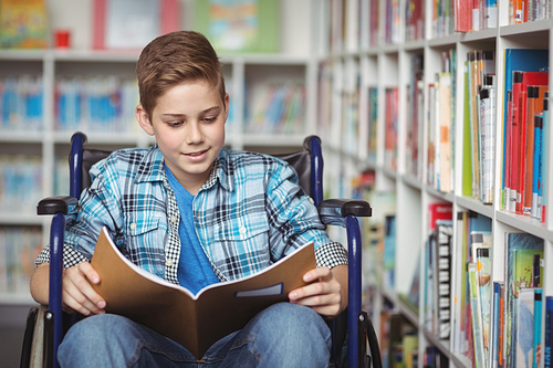 Disabled schoolboy reading book in library at school
