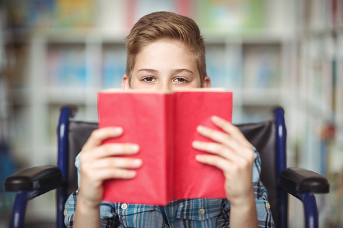 Portrait of disabled schoolboy holding book in library at school