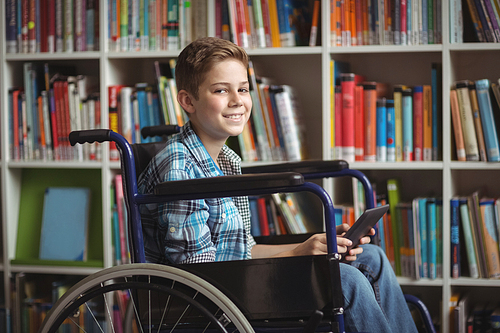 Portrait od disabled schoolboy holding digital tablet in library at school