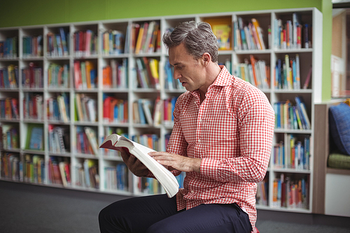 Attentive school teacher reading book in library at school