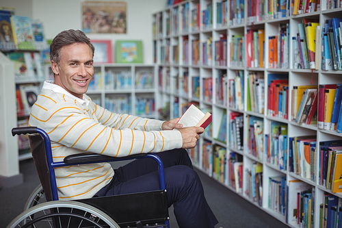 Portrait of disabled school teacher holding book in library at school