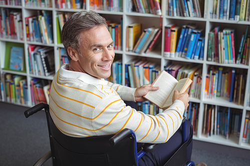 Portrait of disabled school teacher holding book in library at school
