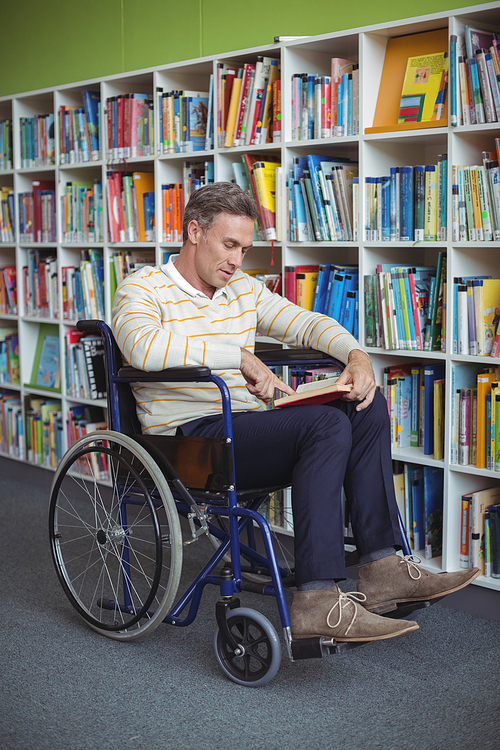 Attentive disabled school teacher reading book in library at school