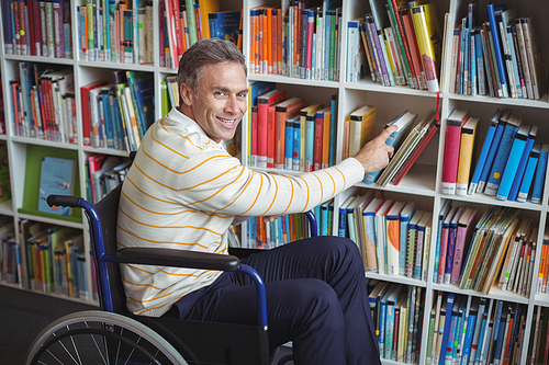 Portrait of disabled school teacher selecting book in library at school
