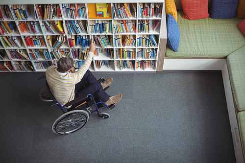Overhead view of disabled school teacher selecting book in library at school