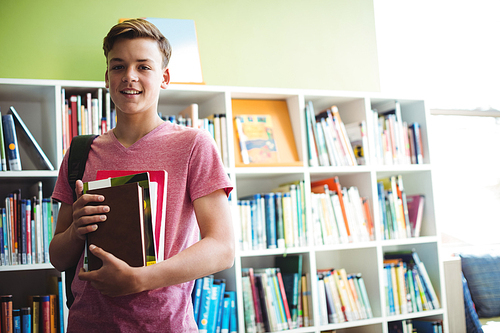 Portrait of happy schoolboy holding book in library at school
