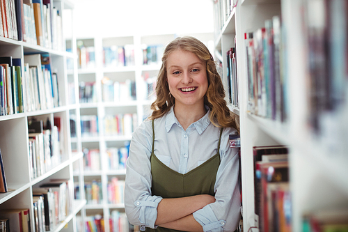 Portrait of schoolgirl standing with arms crossed in library at school