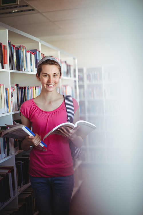 Portrait of happy schoolgirl holding book in library at school