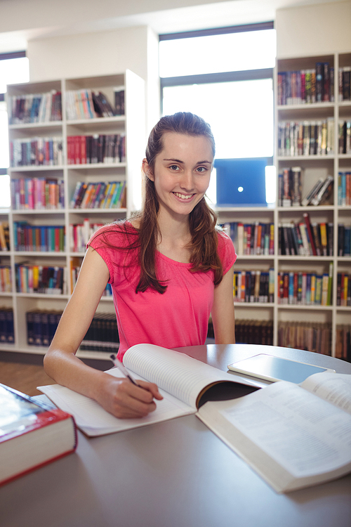 Portrait of smiling schoolgirl doing homework in in library at school