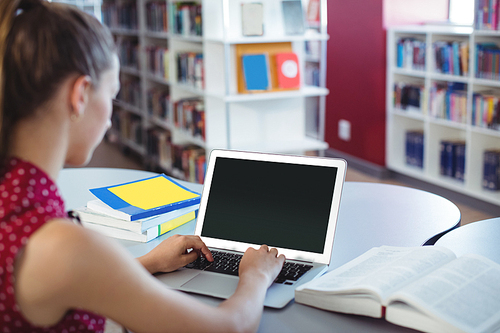 Schoolgirl using laptop in library at school