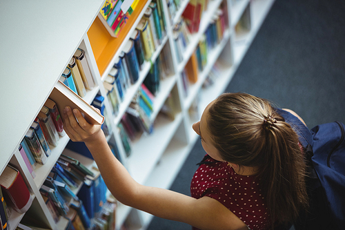 High angle view of schoolgirl selecting book from bookshelf in library at school