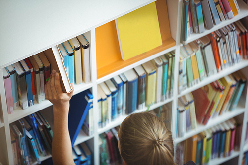 High angle view of schoolgirl selecting book from bookshelf in library at school